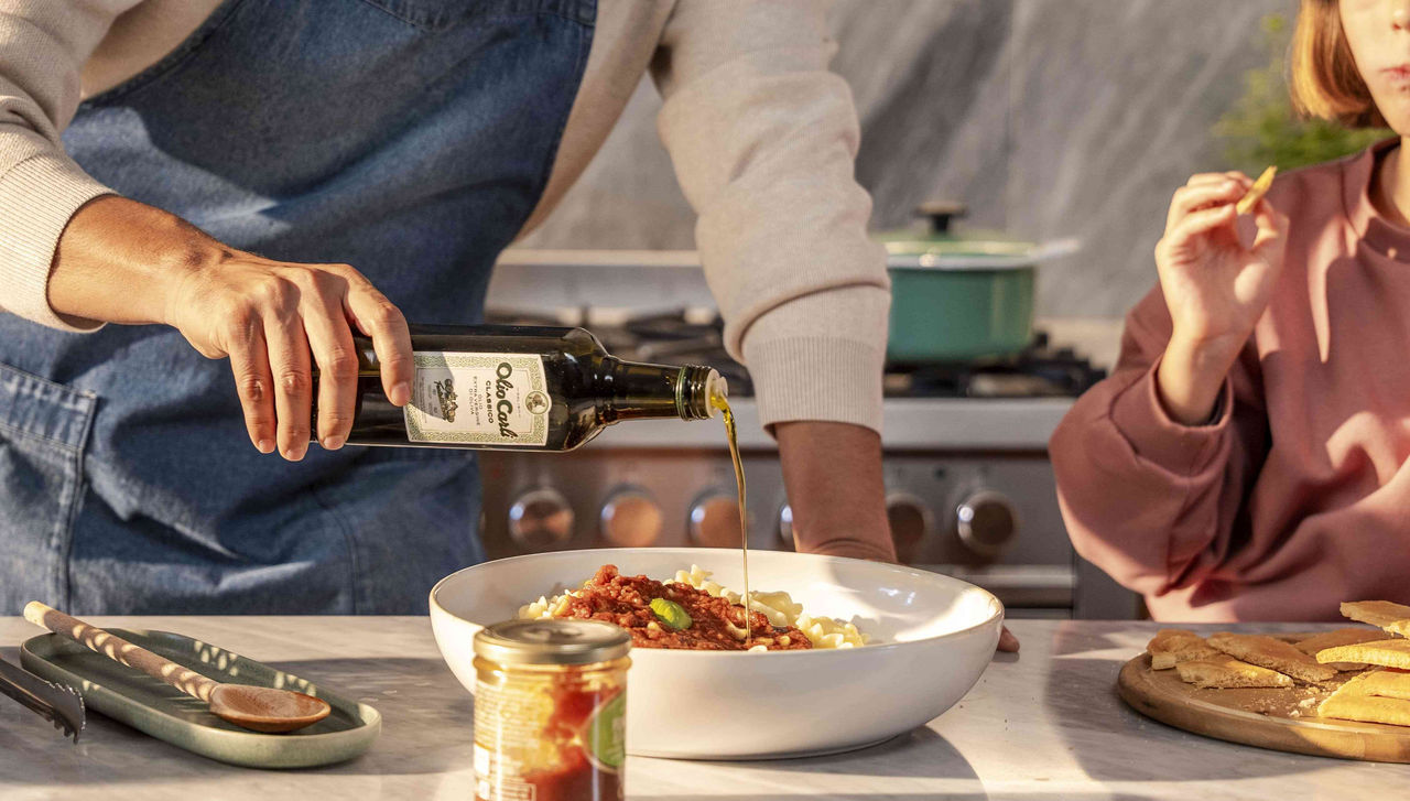 Père et fille à table terminent des pâtes à la sauce avec un filet d’Huile Carli Vierge Extra d’Olive Classique