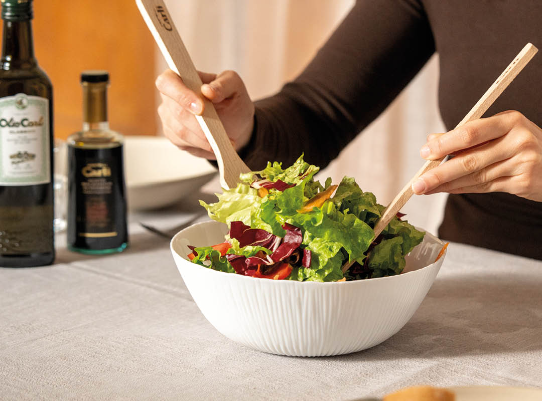 personne qui assaisonne une salade avec de l'huile et du vinaigre