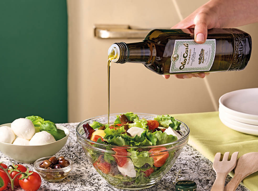 personne qui assaisonne une salade avec de l'huile 