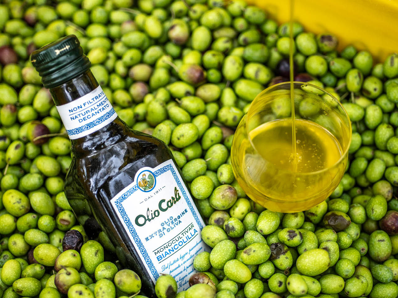 Bouteille d'huile d'olive vierge Biancolilla dans une caisse remplie d'olives